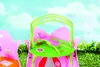 A close-up view of a pink and green toy cottage with a green roof and a pink accessory on a grassy area with a blue sky and clouds in the background. Produktbild-Vorschau