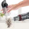 A hand is shown emptying dust from a handheld vacuum cleaner's dustbin onto a surface. Produktbild-Vorschau
