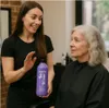 A hairdresser is showing a bottle of Matrix So Silver shampoo to an older woman with gray hair. Produktbild-Vorschau