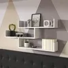 A white floating shelf unit is mounted on a wall with a geometric pattern. The shelves are decorated with various items. Podgląd zdjęcia produktu