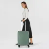 A woman is standing and holding the handle of a green suitcase. Podgląd zdjęcia produktu