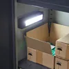 An LED work light illuminates the inside of a metal storage cabinet, with cardboard boxes stacked on a shelf. Produktbild-Vorschau