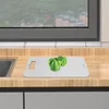 A stainless steel cutting board with two green bell peppers on it, placed on a wooden countertop next to a sink. A window with a view of buildings is in the background. Náhled obrázku produktu