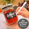 A hand is writing on a label on a jar of strawberry jam. Produktbild-Vorschau