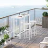 A balcony overlooking the ocean with a white bar table and stools. Produktbild-Vorschau