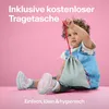A baby sitting on a pink surface, holding a small grey bag with a red string. Anteprima dell’immagine prodotto