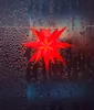 A red star-shaped light decoration hangs on a string against a dark, condensation-covered surface. Produktbild-Vorschau