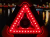 A close-up of a red LED warning triangle with a dark background and blurred lights in the distance. Voir les images du produit