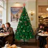 People sitting at tables in a cafe decorated for Christmas with a decorated Christmas tree. Produktbild-Vorschau