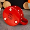 The bottom of a red, polka-dotted ceramic object, possibly a mug or teapot, is shown resting on a textured gray surface. In the background, out-of-focus wooden discs and a glass are visible. Náhled obrázku produktu
