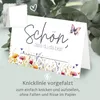 A folded card with floral illustrations and text, set against a blurred background of eucalyptus leaves. Produktbild-Vorschau
