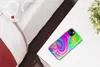 A phone case with a psychedelic pattern rests on a white table next to a bed. Produktbild-Vorschau