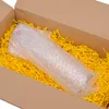 A roll of bubble wrap is placed inside a cardboard box filled with yellow shredded paper. Produktbild-Vorschau