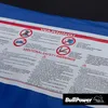 A close-up of a safety warning label on a blue fabric surface, likely a trampoline. Produktbild-Vorschau