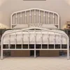 A white metal bed frame with a decorative headboard and footboard, set up in a bedroom with bedding and pillows. Produktbild-Vorschau