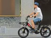 A man rides an electric bicycle down a city street. Produktbild-Vorschau
