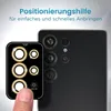 A finger is shown holding a camera lens protector with decorative stones, next to a smartphone's camera module. Produktbild-Vorschau