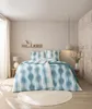 A bedroom scene with a bed made up with a blue and white wave-patterned duvet cover. Produktbild-Vorschau