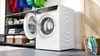 A laundry room with a washing machine, shelves with laundry supplies, and a basket of towels. Produktbild-Vorschau