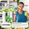 A woman is smiling and holding a glass of green juice next to a steam juicer filled with apples. Náhled obrázku produktu