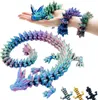 A hand holding a small, crystal-like dragon figurine, with a larger, more elaborate dragon figurine coiled in the foreground. Several smaller dragon figurines are visible at the bottom right. Produktbild-Vorschau
