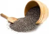 A wooden bowl tipped over, spilling chia seeds onto a white surface, with a wooden scoop nearby. Produktbild-Vorschau