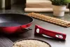 A red frying pan with a detachable handle is shown on a kitchen counter. Produktbild-Vorschau