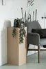 A plant sits on a wooden pedestal next to a gray armchair in front of a brick wall with graffiti. Produktbild-Vorschau
