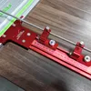 A close-up view of a red aluminum parallel guide system attached to a silver guide rail, resting on a wooden surface. Náhled obrázku produktu