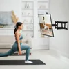 A woman is doing lunges on a yoga mat in a living room, with a TV mounted on the wall displaying a fitness video. Produktbild-Vorschau