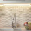 A close-up view of a kitchen sink area, featuring a faucet, soap dispenser, and a bowl of fruit, with a tiled backsplash and under-cabinet lighting. Produktbild-Vorschau