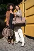 Two women are posing with leopard print duffel bags in front of a yellow shipping container. Náhled obrázku produktu