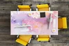 A top-down view of a desk with a colorful watercolor desk mat and yellow chairs. Produktbild-Vorschau