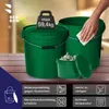 Several green buckets are displayed on a wooden surface, with a hand cleaning one of the buckets. A weight is placed on top of one bucket, and a smaller container filled with garlic is in front of the buckets. Podgląd zdjęcia produktu