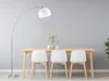 A modern dining area with a floor lamp, a wooden table, and three white chairs. Produktbild-Vorschau
