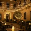 An outdoor courtyard at night, decorated with numerous strings of warm white fairy lights, illuminating tables and chairs set up for dining. Anteprima dell’immagine prodotto