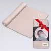 A rolled-up baby swaddle is shown next to its packaging, which is tied with a red ribbon. Náhľad obrázku produktu