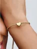A close-up shot of a person's arm wearing a gold bracelet with a heart-shaped charm. Podgląd zdjęcia produktu