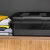 A black storage box with a lid sits on a wooden shelf next to a stack of folded towels. Anteprima dell’immagine prodotto