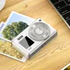 A white digital camera is placed on a wooden desk next to some printed photographs and a laptop keyboard. Produktbild-Vorschau