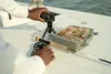 A person's hands are shown setting up a GoPro camera on a tripod on a boat deck, next to a fishing tackle box and fishing rod. Anteprima dell’immagine prodotto