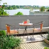 A balcony setting with a table and chairs, overlooking a body of water and distant buildings. Produktbild-Vorschau