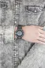 A person wearing a gray denim shirt and a black digital watch. Produktbild-Vorschau