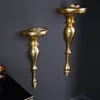 Two ornate gold wall consoles are mounted on a dark gray wall, with a black table and a candle holder in the foreground. Produktbild-Vorschau