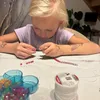 A young girl is making jewelry on a table. Anteprima dell’immagine prodotto