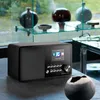 A black internet radio is placed on a dark surface in front of a window with decorative vases on shelves. Produktbild-Vorschau