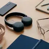 A desk with headphones, a smartphone, glasses, and a notebook. Produktbild-Vorschau