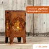 A rusty metal fire pit with a tree of life design, set against a wooden background. Produktbild-Vorschau