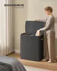 A woman is placing a towel into a dark gray, three-compartment laundry hamper in a bedroom. Náhled obrázku produktu