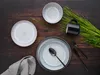 A top-down view of a table setting with plates, cutlery, a mug, and greenery. Produktbild-Vorschau